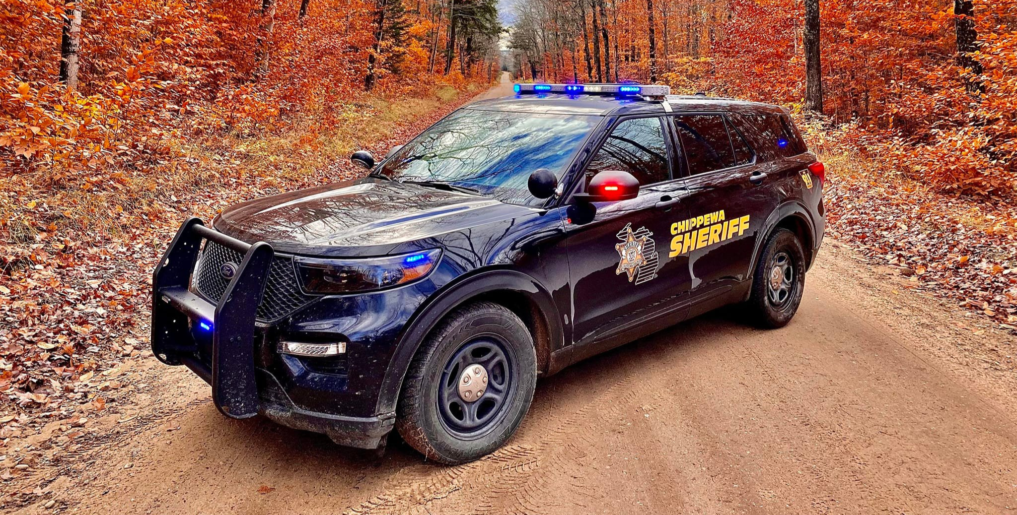 Chippewa County Sheriff SUV on a dirt road lined with autumn trees.