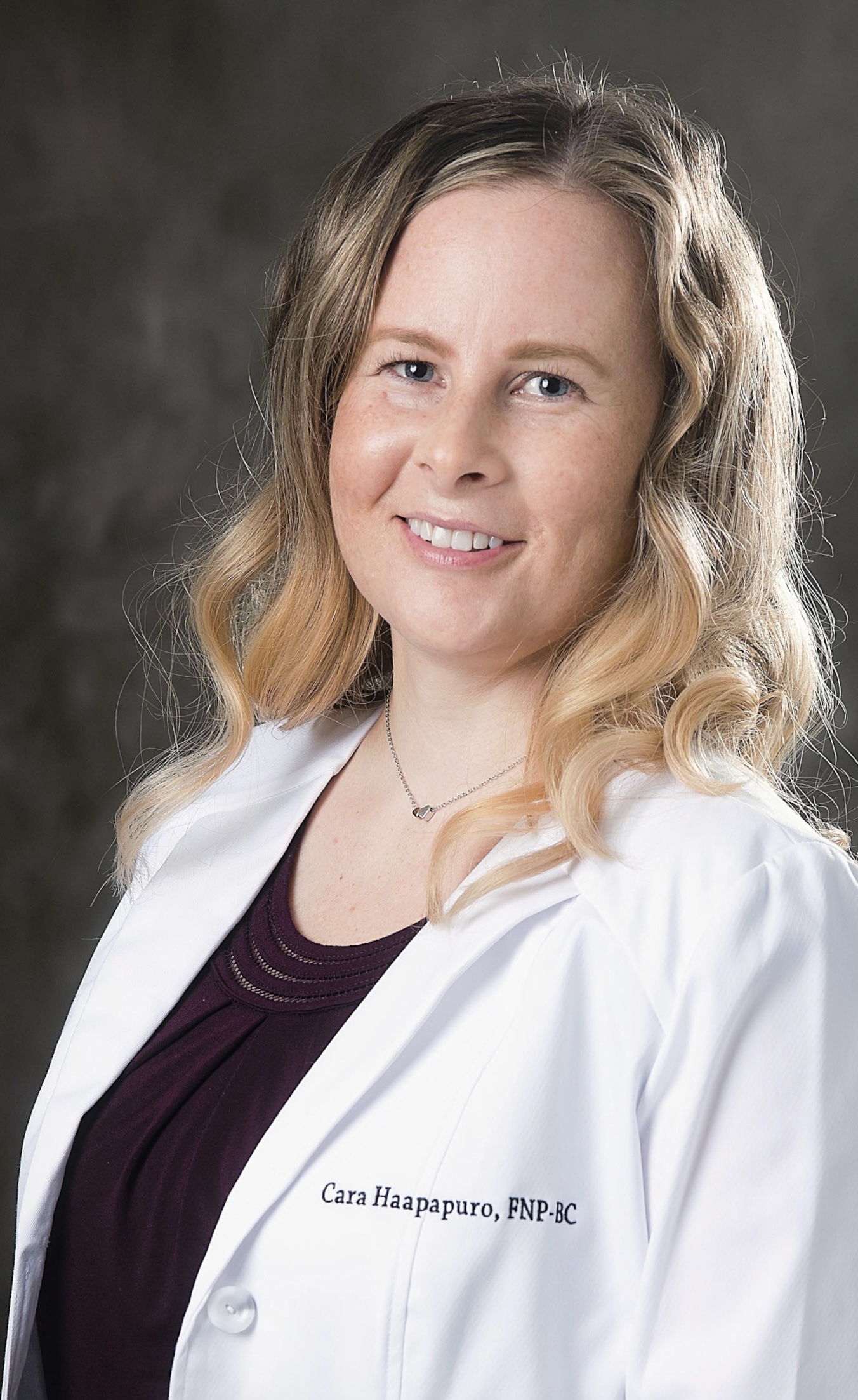 Professional headshot of Cara Haapapuro, FNP-BC, wearing a white medical coat over dark clothing