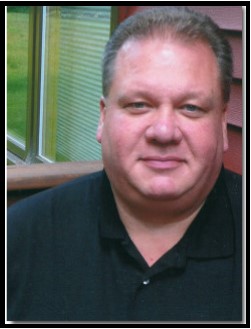 Middle-aged man with gray hair wearing a black polo shirt