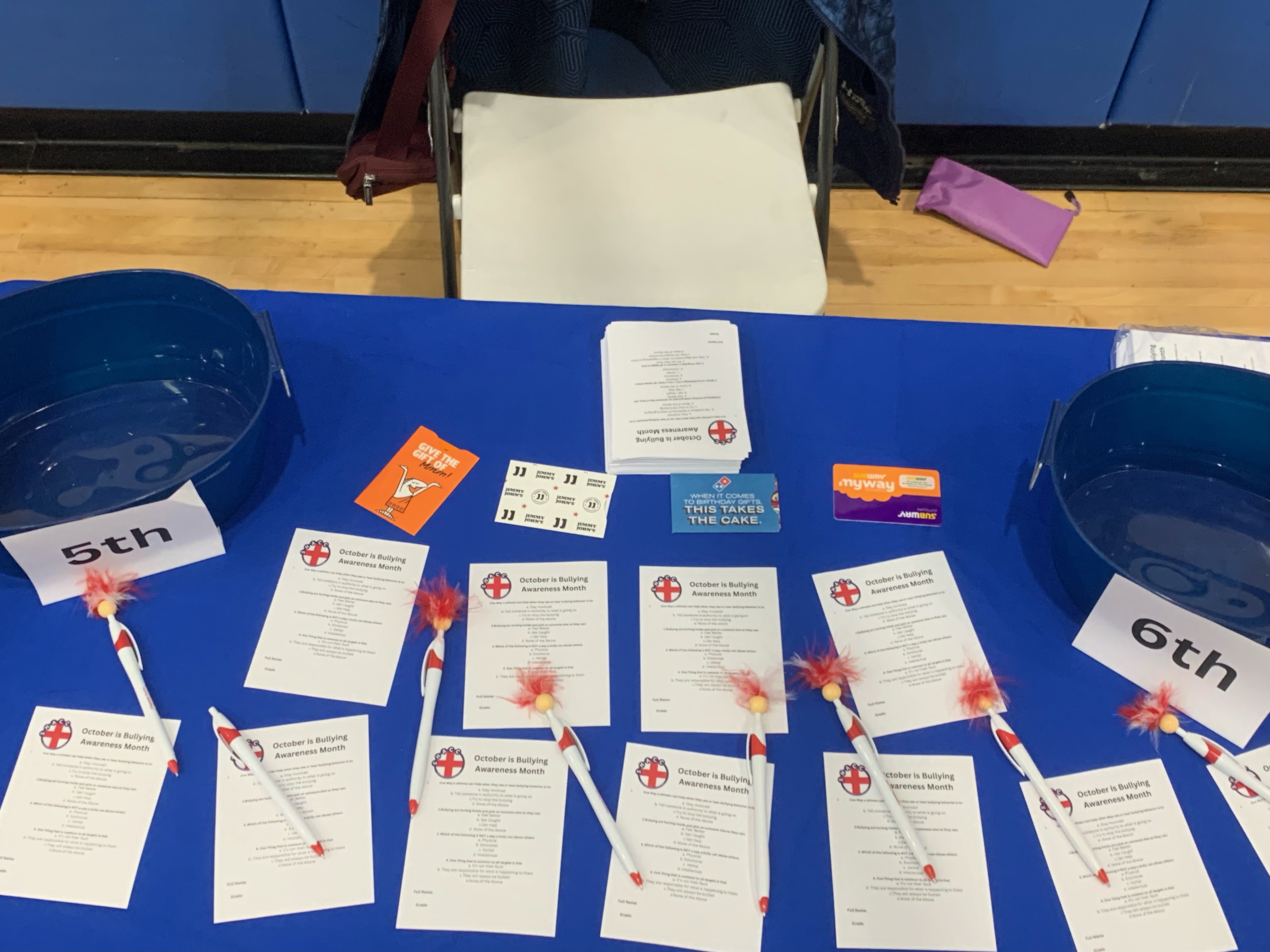 Blue table display with printed materials about October Bullying Awareness Month, promotional cards, and branded items arranged for a county event.