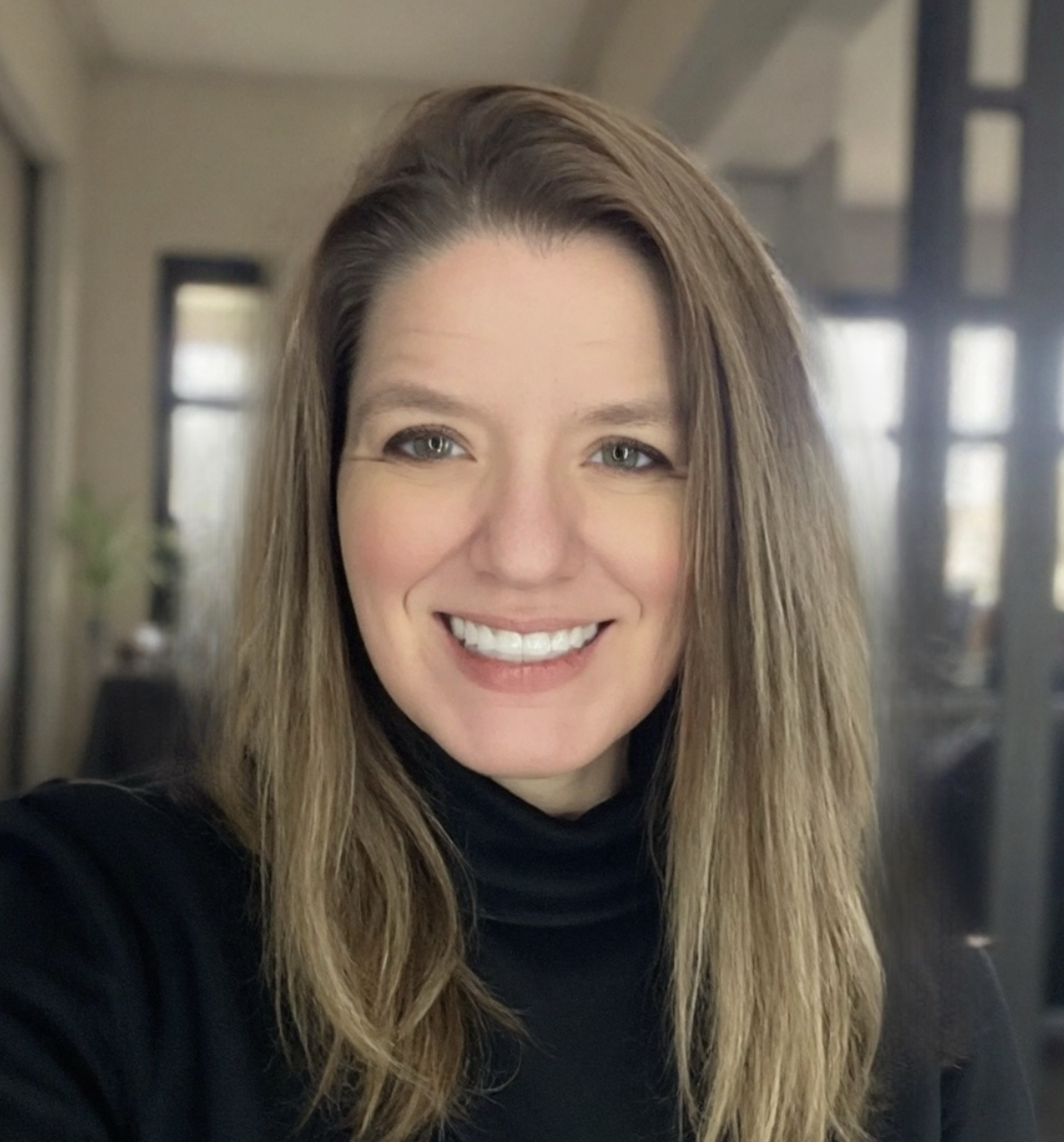 Professional headshot of a woman with long brown hair smiling at the camera in an office setting.