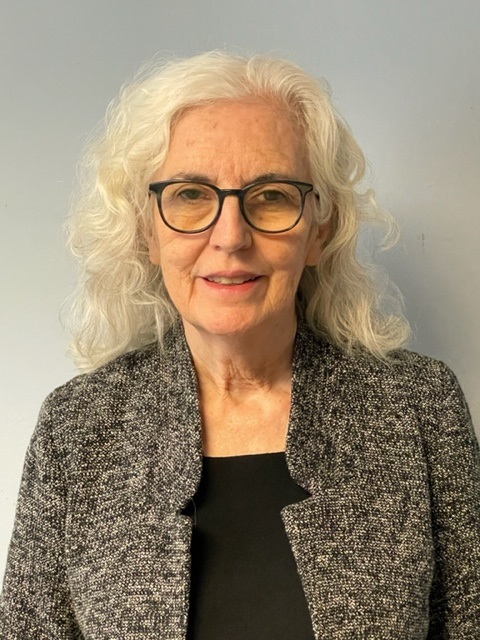 Older woman with long white hair and glasses wearing a gray textured blazer over a black shirt