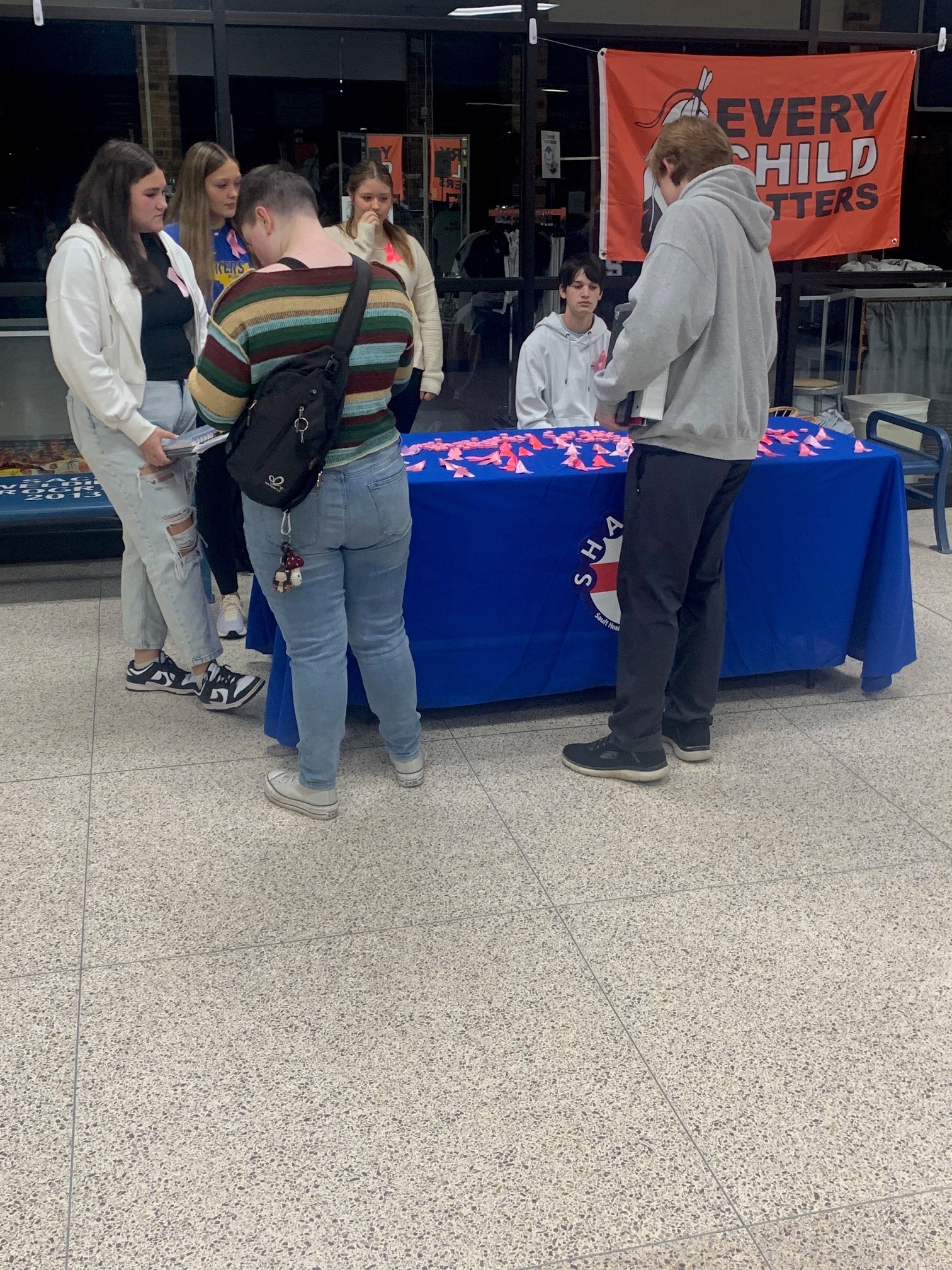 Visitors gather around a blue table at an indoor community event with an 'Every Child Matters' banner displayed on the wall.