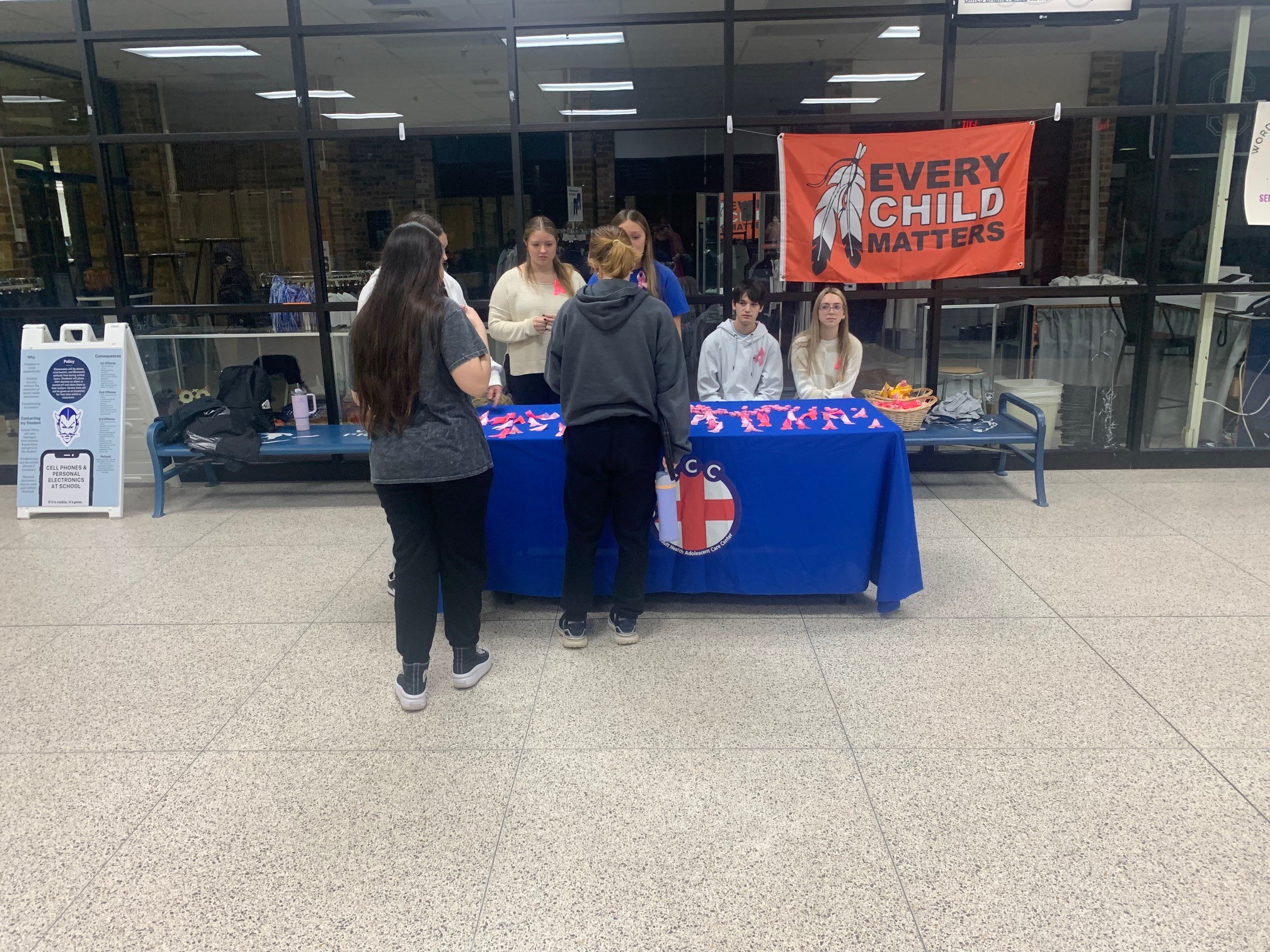 Community members staff an informational booth at an indoor public space with an 'Every Child Matters' banner displayed above.